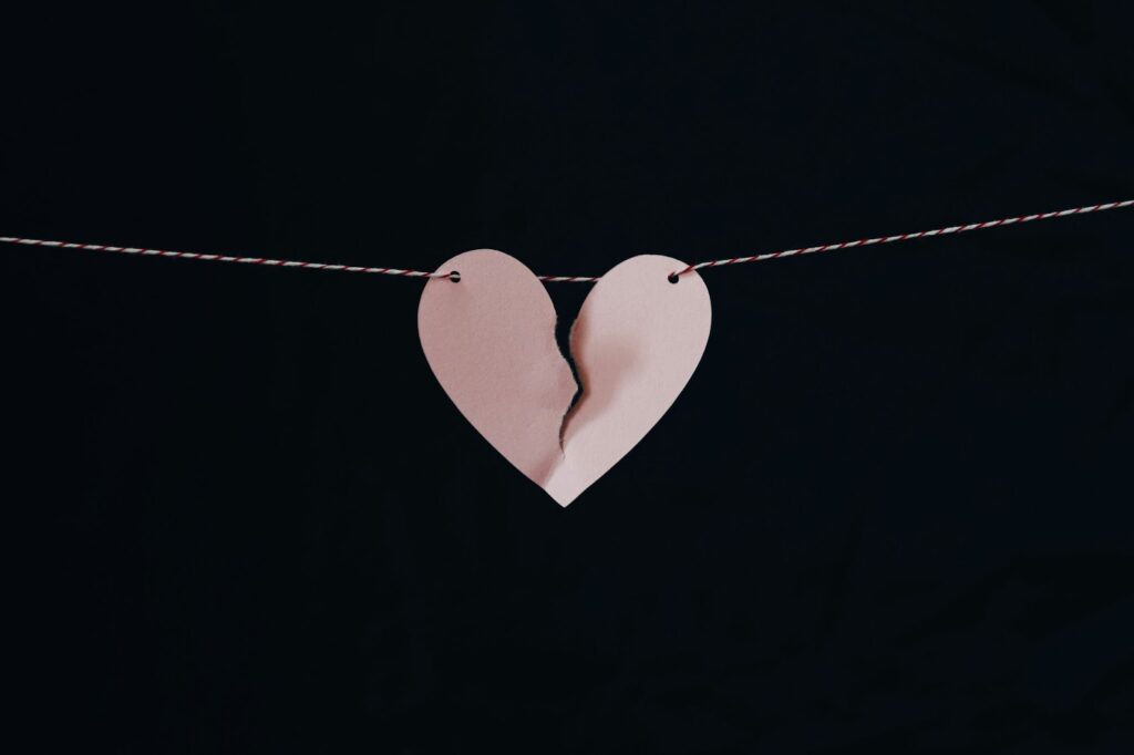 A paper heart hanging with a tear in the middle, symbolizing a broken heart.