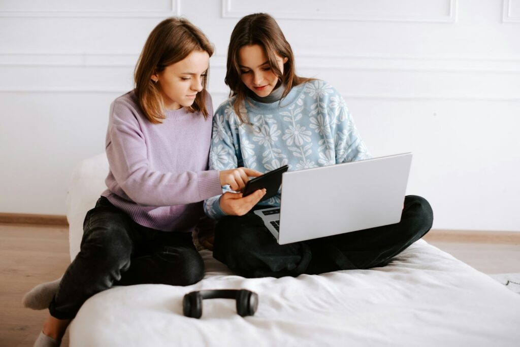 Two teenagers looking at a phone and a laptop together